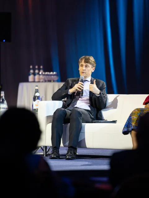 White male and Black woman on a couch on a stage giving a presentation