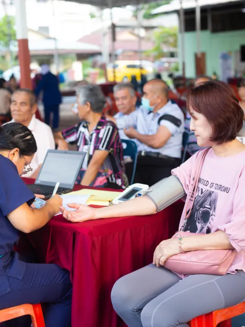 An Asian woman in pink shirt getting her blood pressure measured during a cancer outreach campaign in a public square