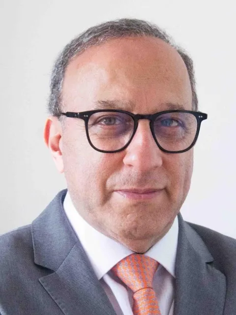 Headshot of Middle Eastern man in a suit with dark glasses and orange tie