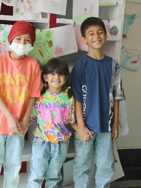 Three children in colorful shirts, one wearing a mask, in a cancer centre for children