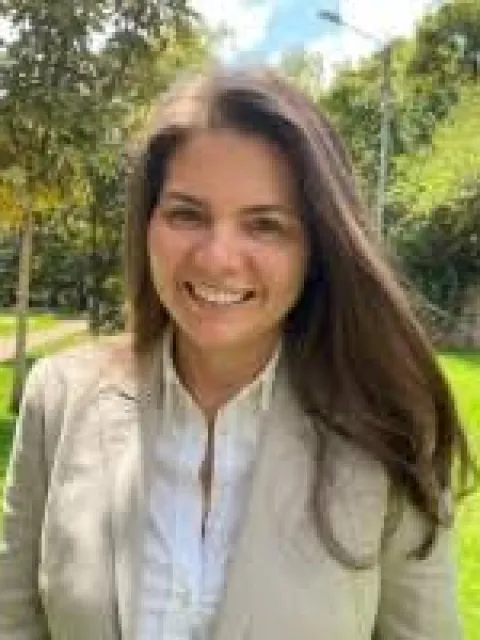 Headshot of Hispanic woman with long dark hair wearing cream blazer with park background