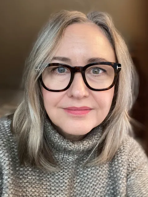 Headshot of middle age White woman wearing roller neck sweater and black glasses