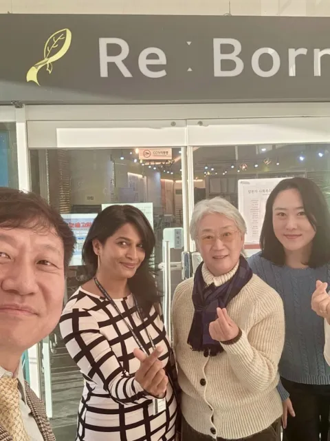 Diverse group featuring one man and four women posing for a picture in front of a sign "Re:Born"