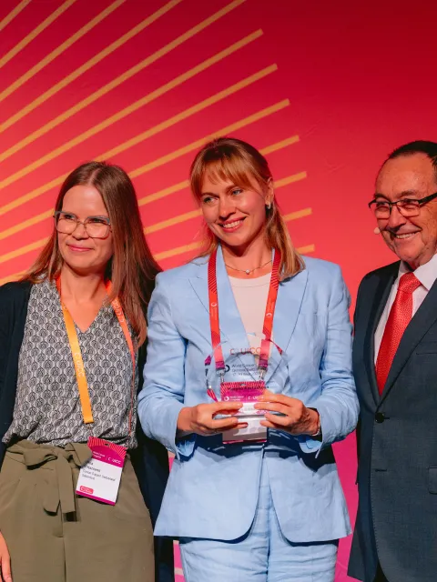 Two women and a man in suit receiving an award on stage
