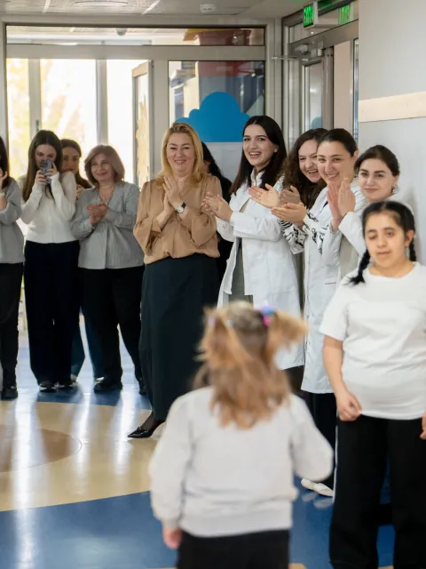 A child with cancer is cheered by the clinicians and health workers as she walks down the hall to ring the remission bell