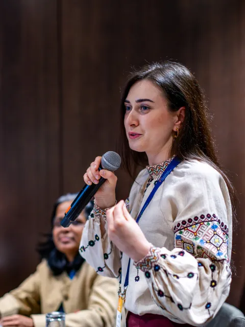 Eastern European woman with black hair speaking into a microphone at a conference.