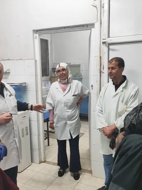 A group of five Middle Eastern and African men and women in hospital setting, 3 in white lab coats, one in blue lab coat, and one women in traditional African dress