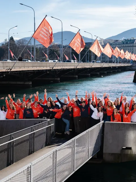 Diverse group of people in World Cancer Day branded hoodies posing outdoors in front a bridge lined with World Cancer Day flags