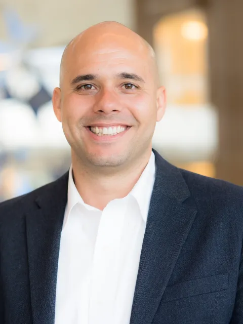 Bald middle-aged white man wearing dark suit coat and white shirt, smiling