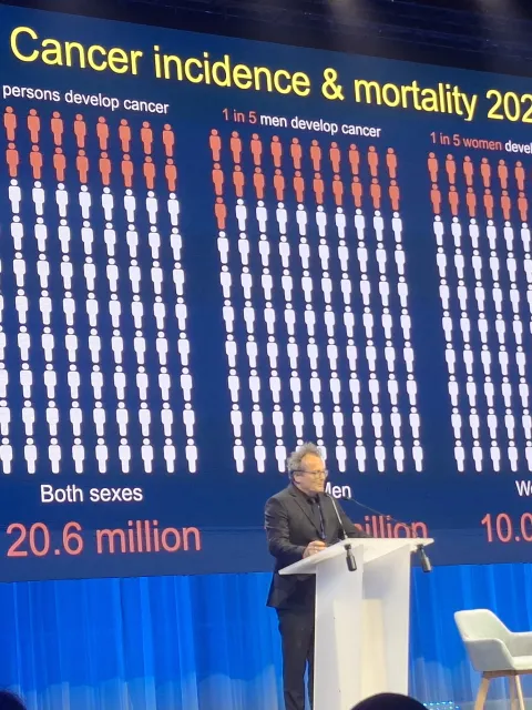 Man at podium giving a slide show presentation of cancer incidence and mortality