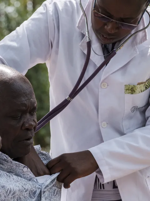 West Kenyan doctor examining an elderly male patient with a stethoscope