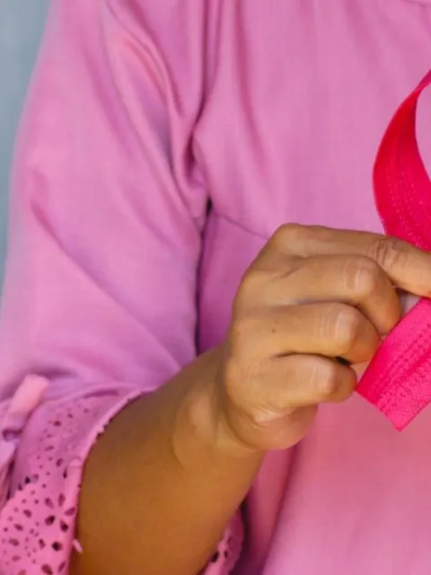 Woman dressed in pink holding a pink ribbon, symbolising breast cancer awareness month