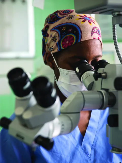 Medical practitioner looks into microscope, to suggest the power of and need for innovation to reduce the burden of cancer