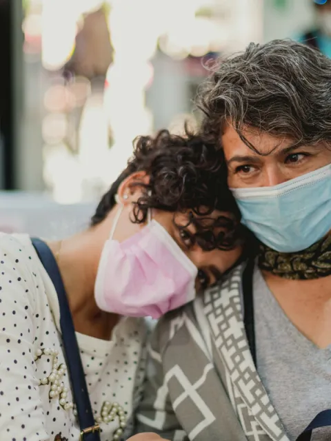 A woman rests her head on the shoulder of another woman, both wearing masks, in a breast cancer clinic in Mexico.