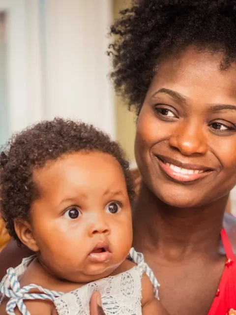 Black woman smiling, with child on her lap. Photo by Andrae Ricketts on Unsplash.
