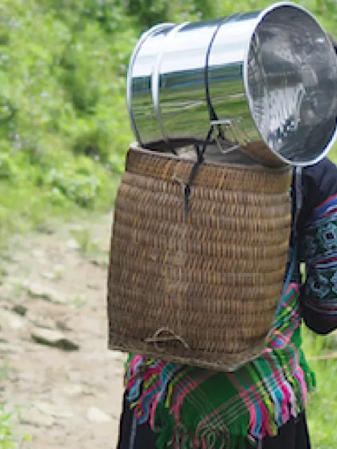 Three women carrying baskets on their back, walking on a mountain trail 