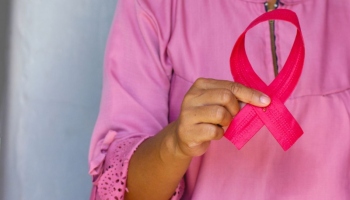 Woman dressed in pink holding a pink ribbon, symbolising breast cancer awareness month
