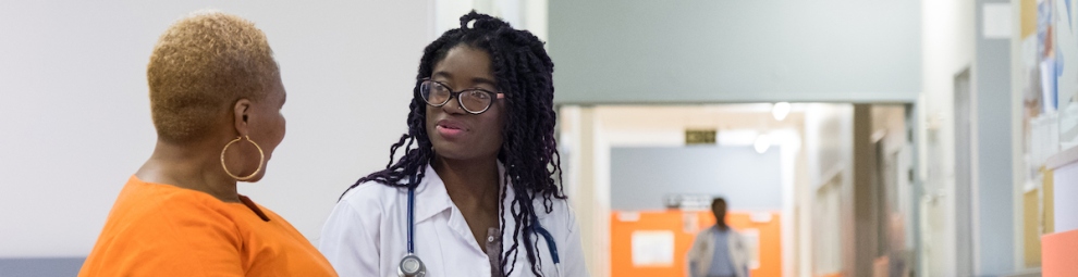A Black woman doctor speaking with a female patient in a hospital hallway