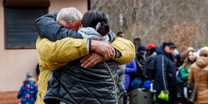 Man and women hugging before a line of Ukrainian refugees