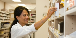 Woman in white blouse reaching for medication on a shelf