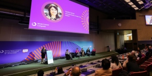Speaker in front of a large auditorium below a big screen, at UICC's World Cancer Congress in Geneva in 2022
