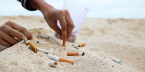 Close up of a person's hand putting out a cigarette in the sand next to other cigarette butts
