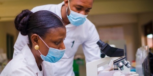 African female and male health care researchers working in life science laboratory, preparing and analysing microscope slides in a research lab